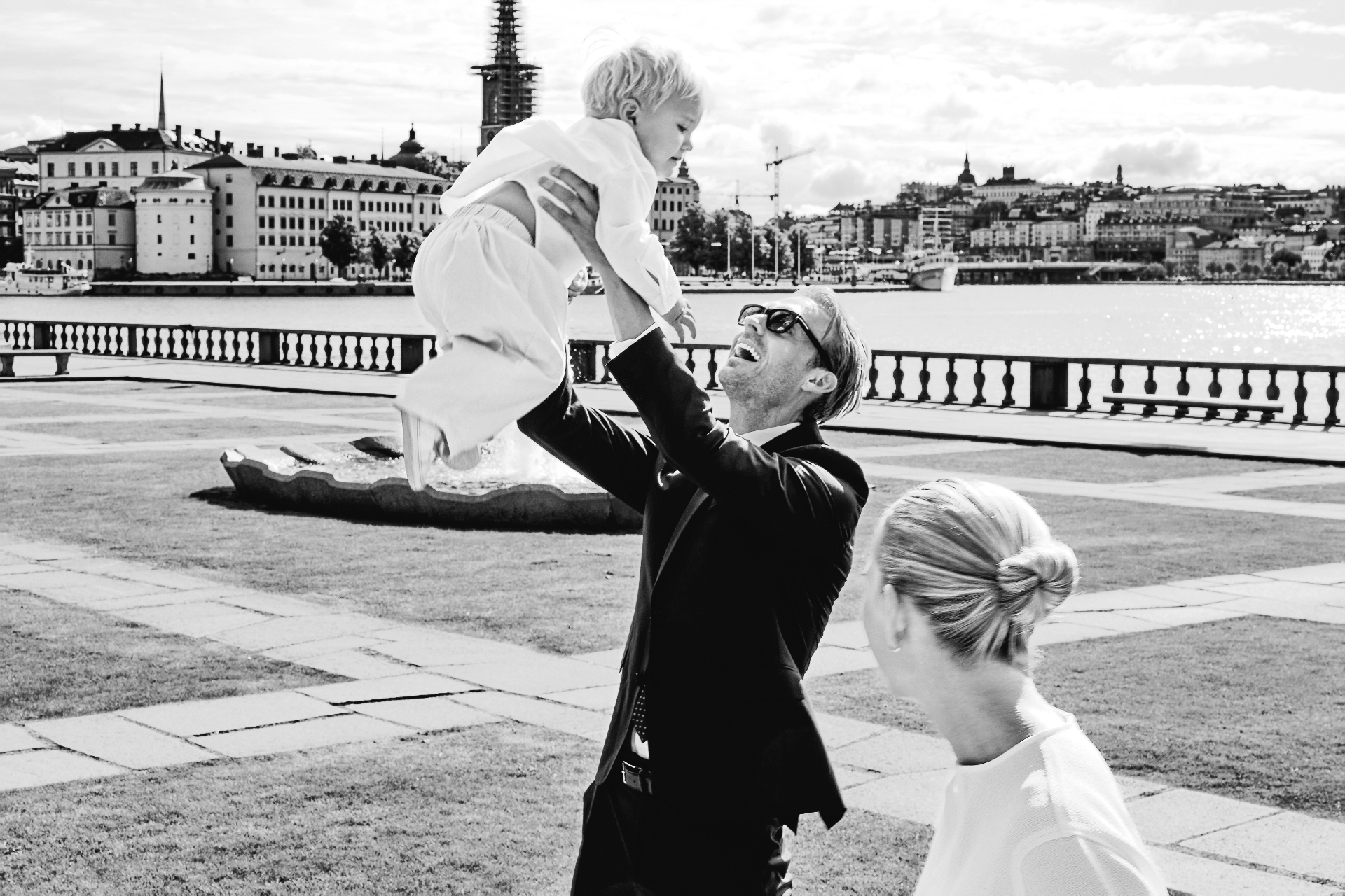 The groom lifting their son into the air by the water