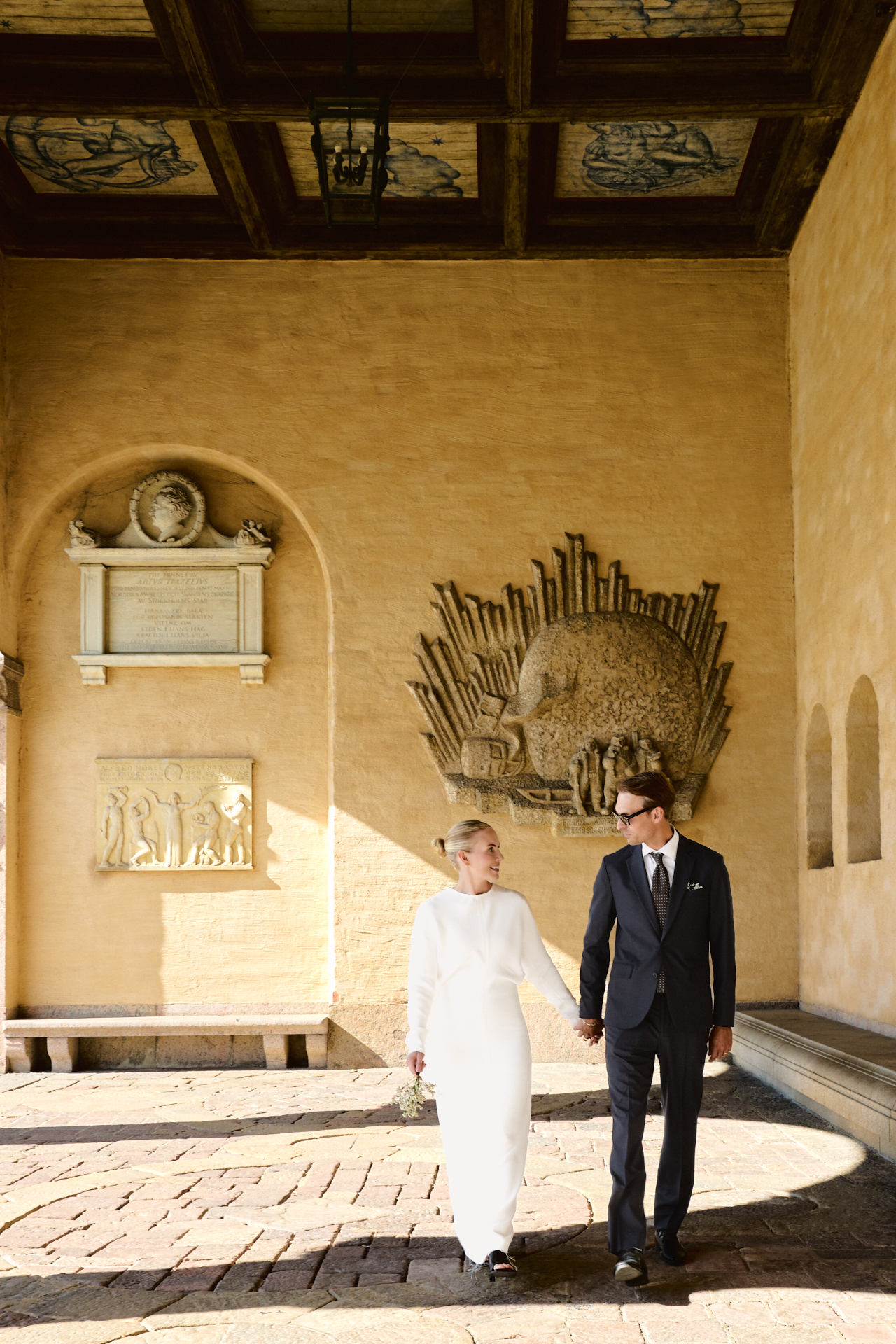 Elin and Simon walking through the courtyard beneath the stone reliefs