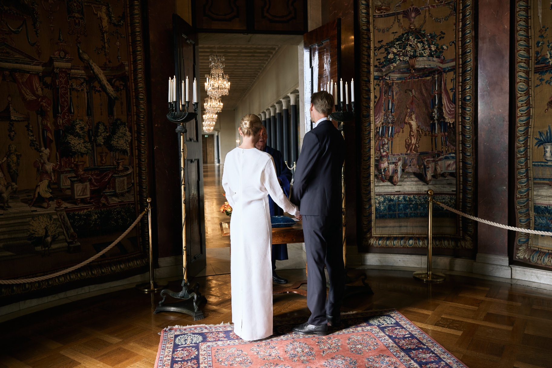 The couple before the officiant in the tapestry hall